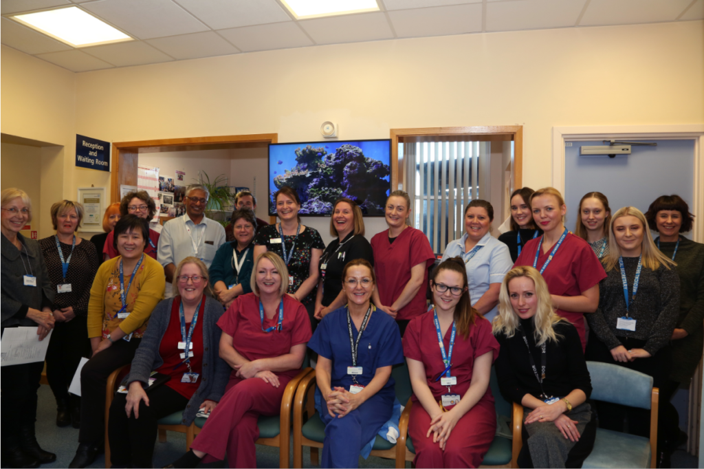 Ipswich Hospital skin conditions team wearing various uniforms sitting and standing together at the reception area.
