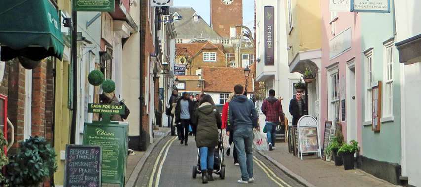 A street with shops in Colchester with people walking through the town. 