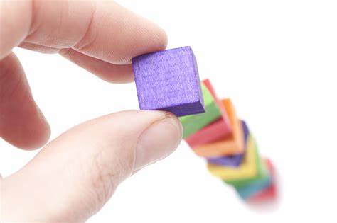 Close up of fingers placing a small purple wooden block on a tower of colourful blocks.