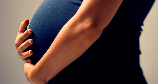 Torso of a pregnant person wearing a navy blue top.