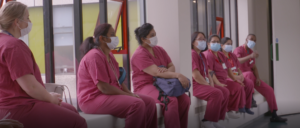 shift handover at Colchester Hospital. Staff dressed in raspberry scrubs, seated near windows.