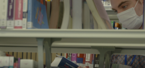 Photo of a bookshelf in a library with a person wearing a face mask reading a book