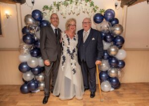 Wedding photo with balloon arch and two men with bride in middle