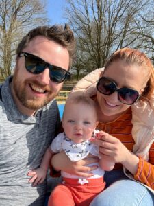 Man and woman in sunglasses smiling at camera holding a little baby