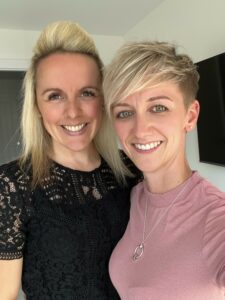 Two women smiling at camera. One with short blond hair, one with long blond hair