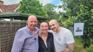 Woman and two men all with shaved heads looking and smiling at camera
