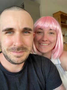 Close up of a man and woman with pink wig close behind him