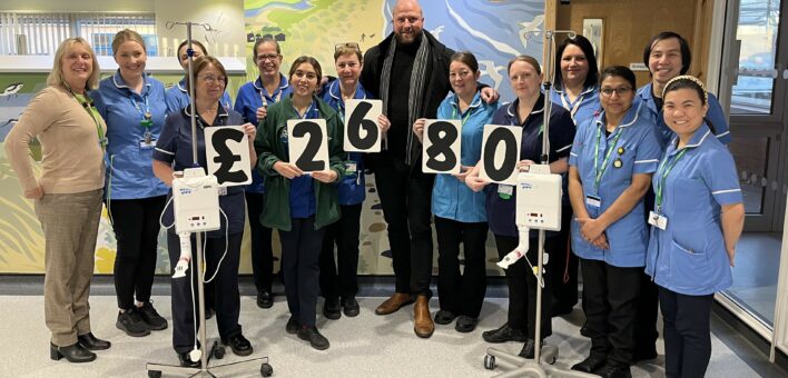 A man with a group of hospital staff wearing uniforms. They hold up cards spelling out "£2680"