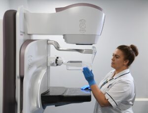 Woman in white clinical outfit next to white machine.