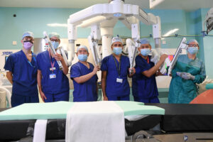 Clinicians in masks in operating theatre standing by a bed and machine