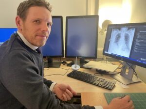 man looking at camera with computer screen of x-ray by him