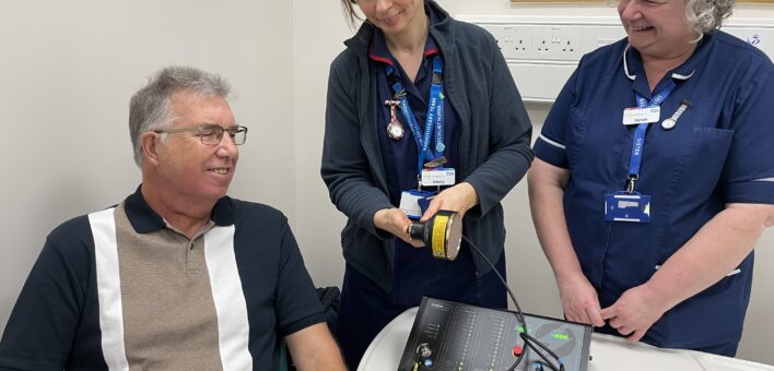 Two NHS nurses show a male patient how the new PBM light therapy machine works