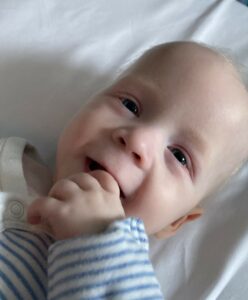 Baby boy Rycroft Alport Foster smiling in his cot