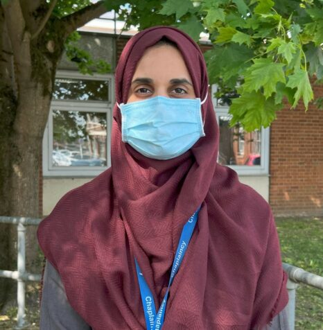 Faiza Hussain standing outside under a tree wearing a face mask.