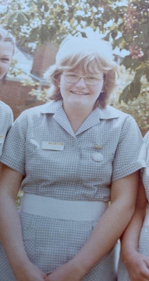 A nurse in NHS uniform sitting down smiling