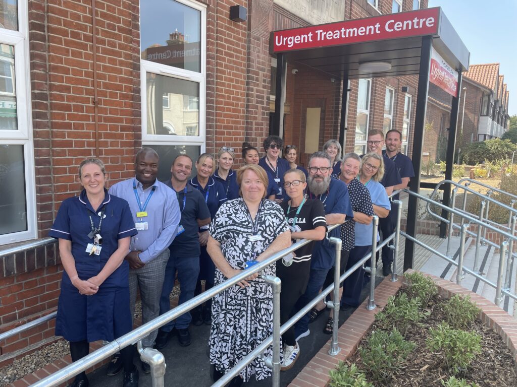 A group of NHS staff stand together outside an urgent treatment centre building