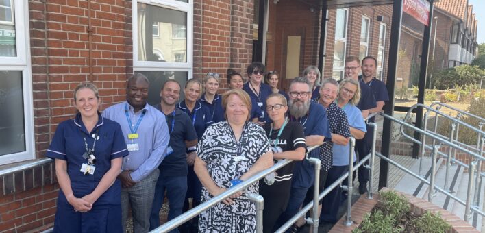 A group of NHS staff stand together outside an urgent treatment centre building